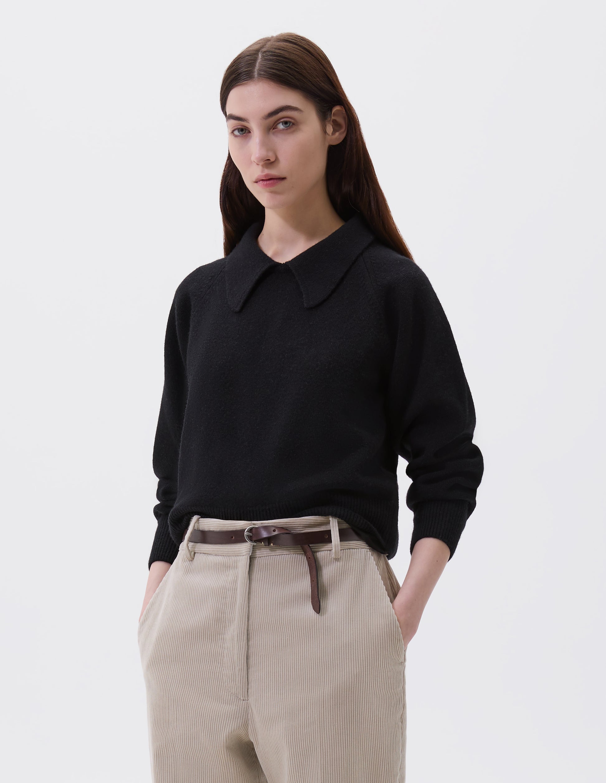 Cropped body image, front view of female model wearing dark brown slim leather belt with sterling silver buckle and contrast hand tack detail. Styled with black collared jumper and beige corduroy trousers.