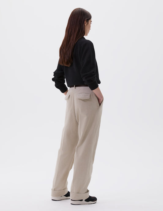 Full body image, back view of model wearing beige corduroy long leg trousers, with belt loops and concealed button fastening flap back pocket. Styled with black jumper, brown leather belt and black and brown trainers.