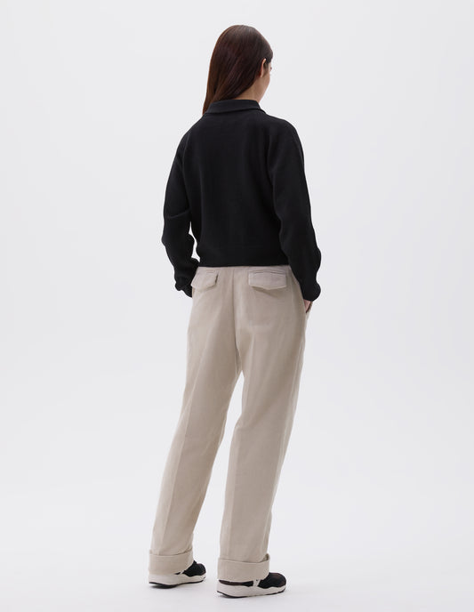 Full body image, back view of model wearing black cropped collared jumper with contrast rib on cuffs and hem. Styled with beige trousers with flap back pockets and black, brown and white trainers.