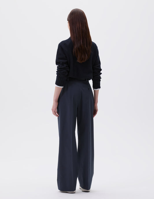 Full body image, back view of model wearing relaxed dark blue and grey striped trousers with straight leg and welt button-through back pocket. Styled with dark blue roll neck jumper and black, brown and white trainers. 