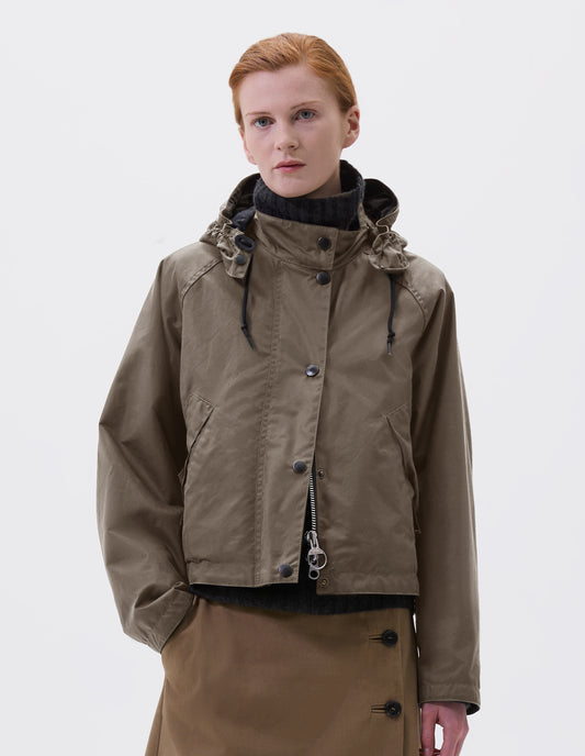 Cropped image, front view of model wearing boxy dark beige jacket with stand collar and hood with wire adjustable peak, raglan sleeve, two-way zip fastening, press stud storm flap and wide storm welt side pockets. Styled over dark grey roll neck jumper and beige midi skirt