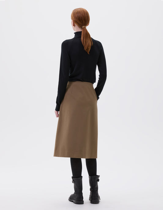 Full body image, back view of model wearing a beige knee length skirt, with concealed side pockets. Styled with with long sleeve black turtleneck jumper, black tights and black leather boots.