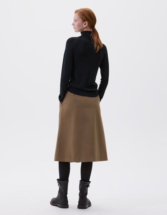 Full body image, back view of model wearing black fine knit merino wool jumper, with high neck, raglan sleeve and cast off edging on neck, cuffs and hem. Styled with brown skirt, black tights and black leather boots.