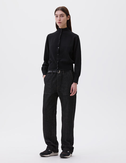 Full body image, front view of model wearing black mock neck cardigan with horn shirt buttons, ribbed collar, cuffs and hem. Styled with black jeans, black leather belt and black, brown and white trainers.