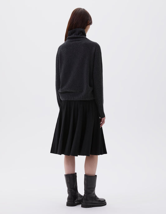 Full body image, back view of model wearing charcoal grey high neck cashmere jumper, with saddle sleeve and contrasting wide rib on neck, cuffs and hem. Styled with knitted black pleat skirt and black leather boots.