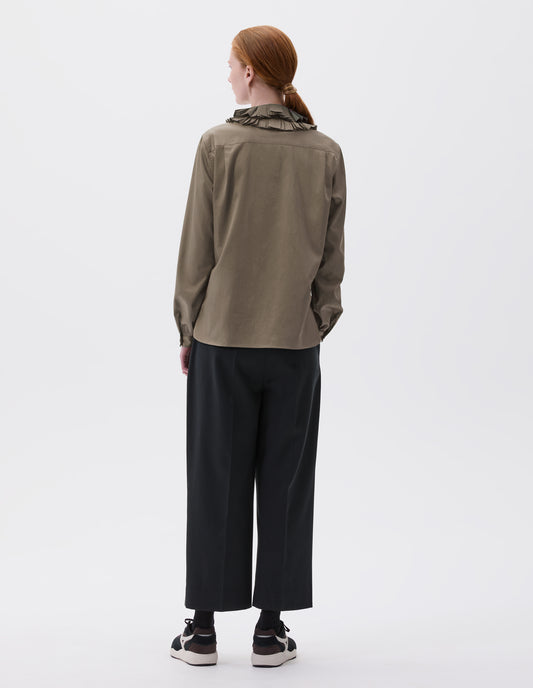 Full body image, back view of model wearing dark green long sleeve shirt with with ruffled collar and shirt cuffs. Styled with cropped black trousers, black socks and black and brown trainers.