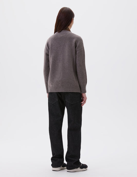 Full body image, back view of model wearing beige v-neck cardigan, with contrast rib cuffs and hem.  Styled with black denim jeans and black and brown trainers.