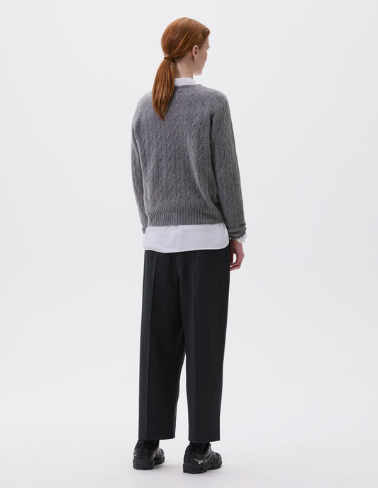 Full body image, back view of model wearing grey cable knit long sleeve jumper with raglan sleeve and contrast rib on neck, cuffs and hem. Styled with black cropped trousers, white shirt and black trainers.