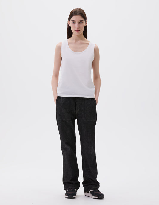 Full body image, front view of model wearing off white cotton sleeveless vest with scoop neck. Styled with black denim jeans and black and brown trainers.