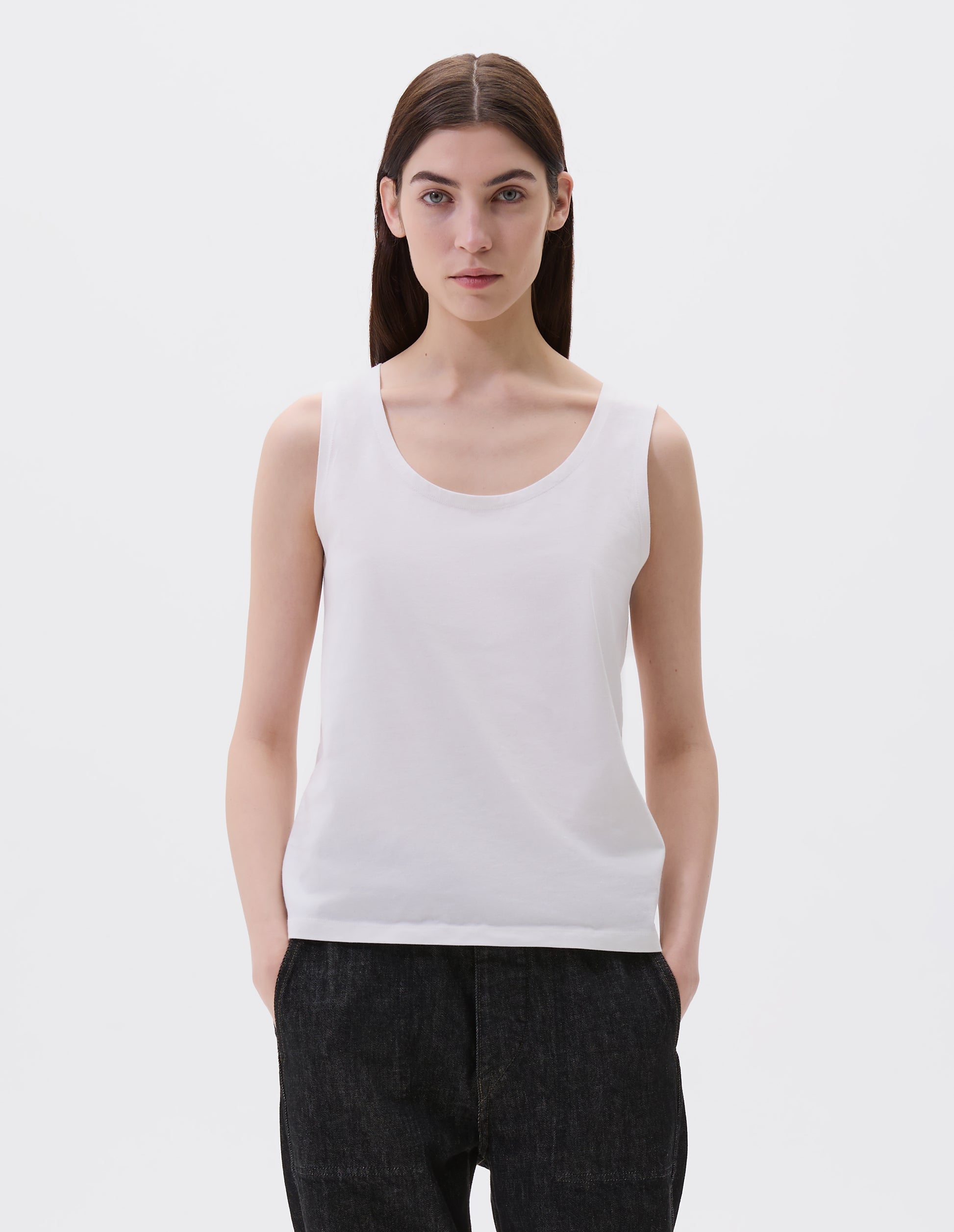 Cropped body image, front view of model wearing off white cotton sleeveless vest with scoop neck. Styled with black denim jeans.