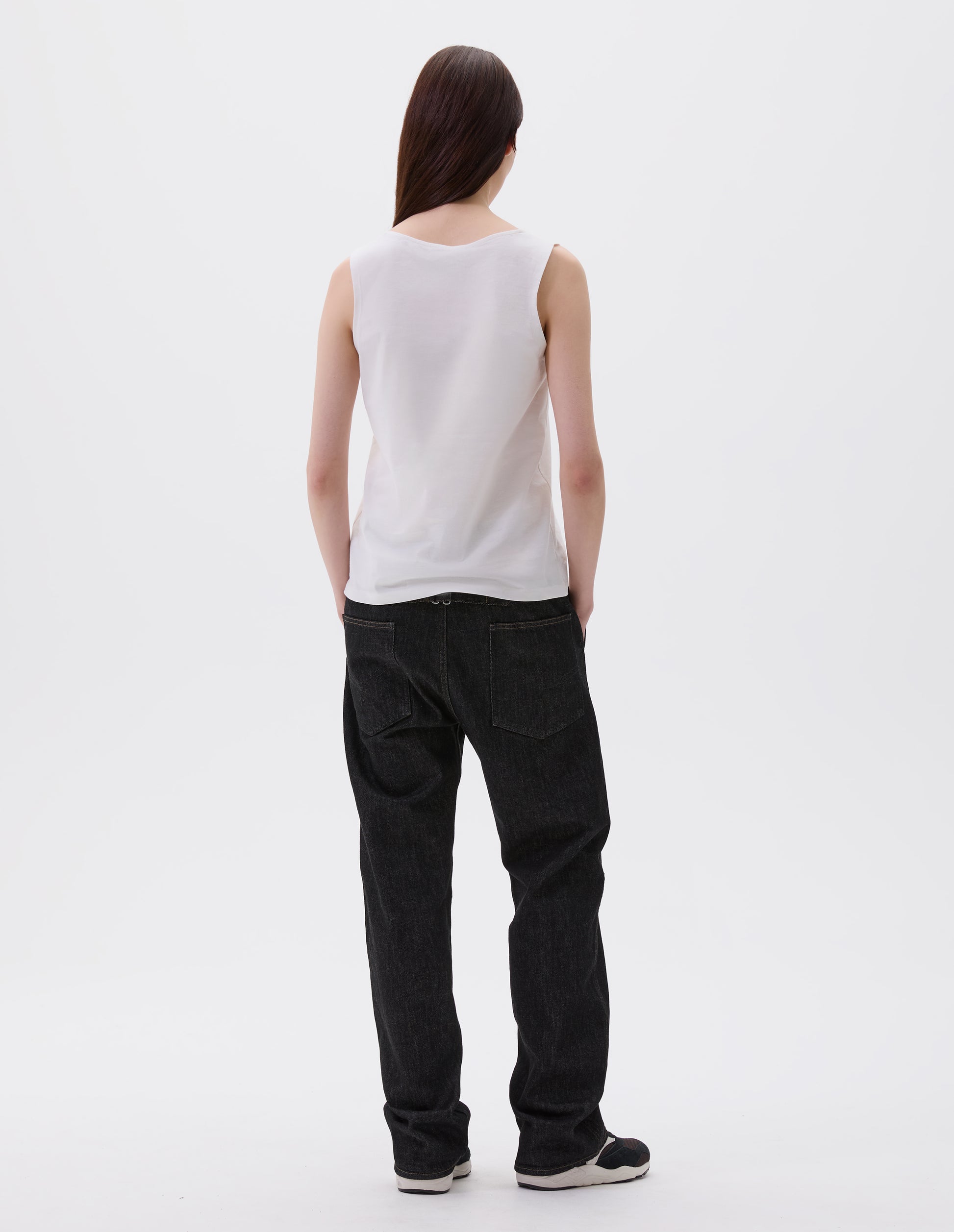 Full body image, back view of model wearing off white cotton sleeveless vest, Styled with black denim jeans and black and brown trainers.
