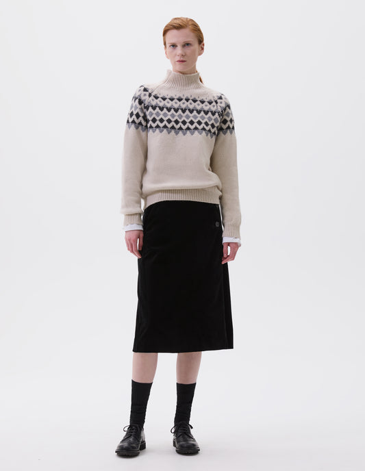 Full body image, front view of model wearing ecru and grey fair isle jumper with inset sleeve and contrasting rib on high neck, cuffs and hem. Styled over white long sleeve, with black velvet skirt, black socks and black leather brogues. 