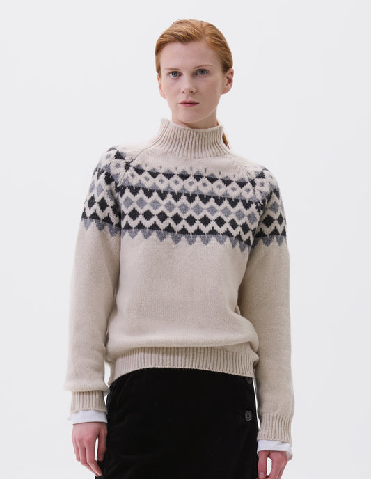 Cropped body image, front view of model wearing ecru and grey fairisle jumper with inset sleeve and contrasting rib on high neck, cuffs and hem. Styled over white long sleeve, with black velvet skirt.