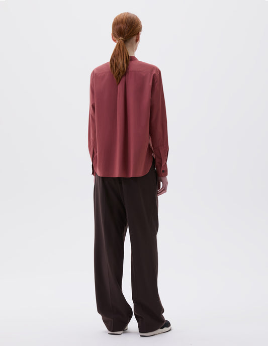 Full body image, back view of model wearing red pink long sleeve collarless shirt with box stich on back yoke and horn button cuffs. Styled with brown trousers and black and brown trainers.  