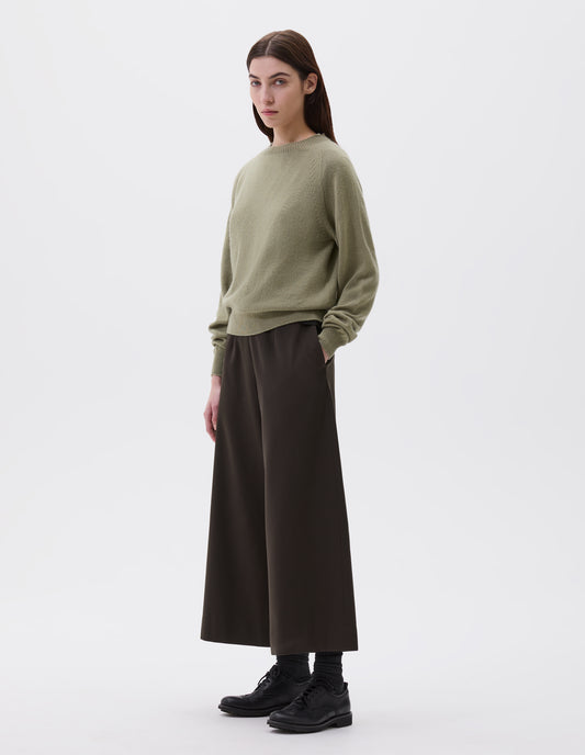 Full body image, front view of model wearing light green long sleeve cashmere jumper, with raglan sleeve and contrasting rib on neck, cuffs and hem. Styled with brown wide leg culottes, black socks and black leather brogues.