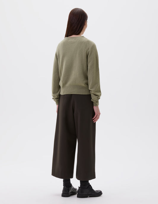 Full body image, back view of model wearing light green long sleeve cashmere jumper, with raglan sleeve and contrasting rib on neck, cuffs and hem. Styled with brown wide leg culottes, black socks and black leather brogues.
