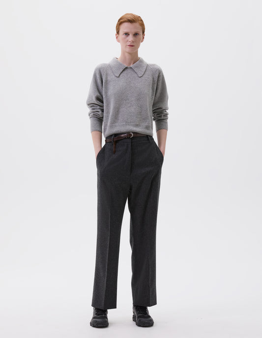 Full body image, front view of model wearing charcoal grey wool trousers with slant side pockets, belt loops and concealed zip fastening. Styled with grey collared jumper, brown slim leather belt and black trainers.