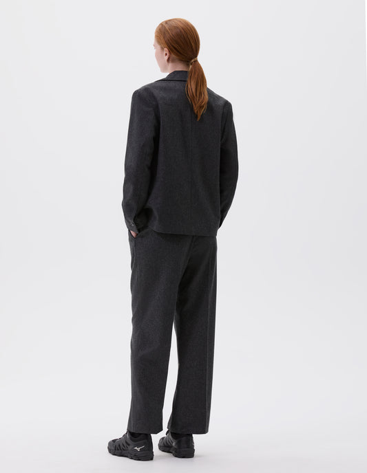 Full body image, back view of model wearing dark grey blazer with horn buttons on cuffs. Styled with matching trousers and black trainers. 