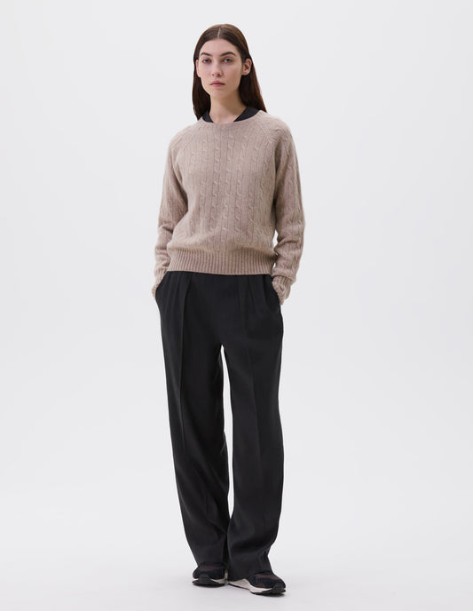 Full body image, front view of model wearing beige cable knit long sleeve jumper with raglan sleeve and contrast rib on neck, cuffs and hem. Styled with black shirt, black trousers and black and brown trainers.