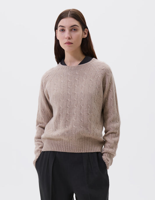 Cropped body image, front view of model wearing beige cable knit long sleeve jumper with raglan sleeve and contrast rib on neck, cuffs and hem. Styled with black shirt and black trousers.