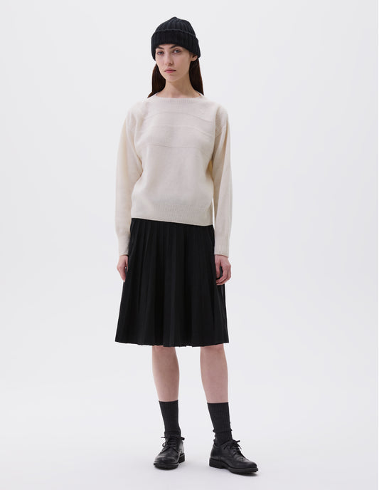Full body image, front view of model wearing ecru crew neck jumper with textured panelling on shoulders and chest and contrasting rib on neck, cuffs and hem. Styled with black rib beanie, black knitted skirt, black socks and black leather brogues.