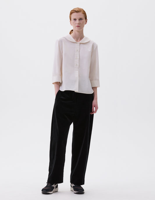 Full body image, front view of model wearing relaxed high waisted black trousers with side pockets. Styled with beige shirt and black, brown and white trainers.