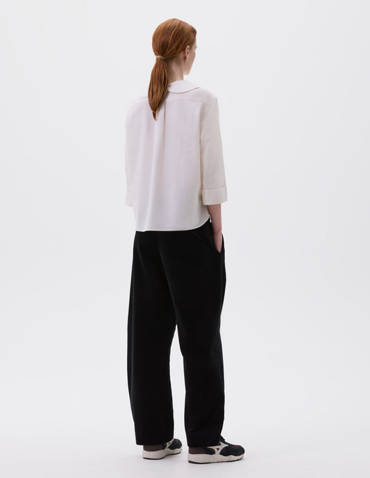 Full body image, back view of model wearing relaxed  high waisted black trousers with side pockets. Styled with beige shirt and black, brown and white trainers.