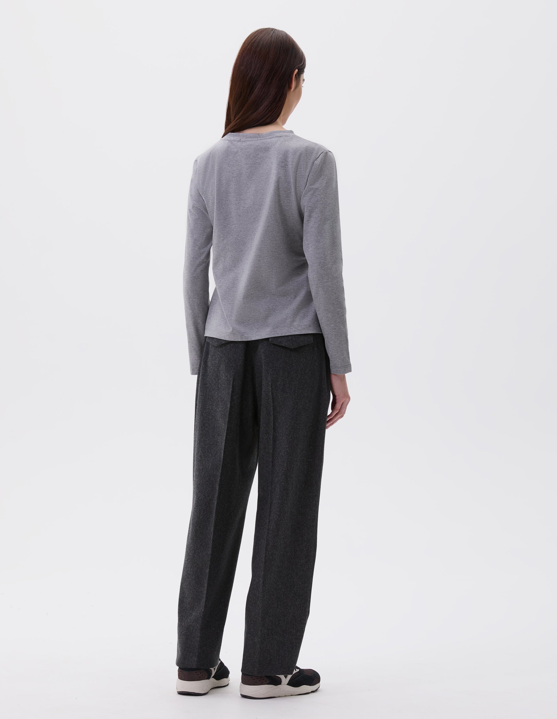 Full body image, back view of model wearing grey cotton wide neck long sleeve with boxy cut. Styled with charcoal grey trousers and black and brown trainers.