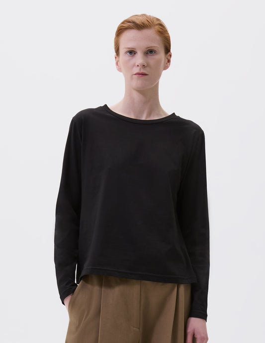 Cropped body image, front view of model wearing black cotton wide neck long sleeve with boxy cut. Styled with brown trousers.