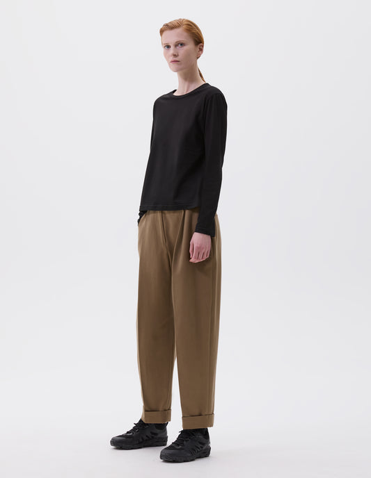 Full body image, front view of model wearing black cotton wide neck long sleeve with boxy cut. Styled with brown trousers and black trainers.