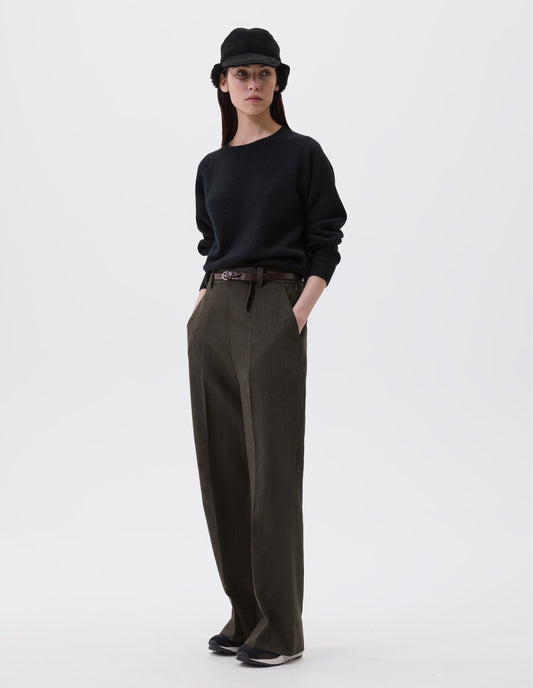 Full body image, front view of model wearing relaxed brown trousers with straight leg, belt loops, side zip and side pockets. Styled with black shearling cap, black jumper, brown leather belt and black, brown and white trainers. 