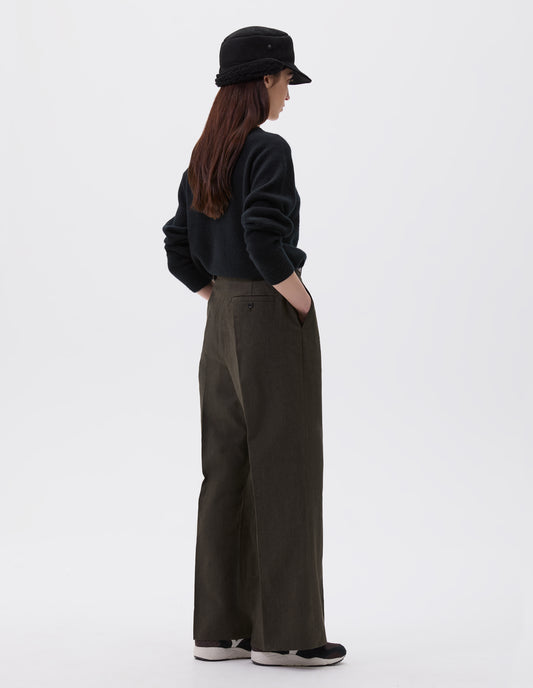 Full body image, back view of model wearing relaxed brown trousers with straight leg and welt button-through back pocket. Styled with black shearling cap, black jumper and black, brown and white trainers.