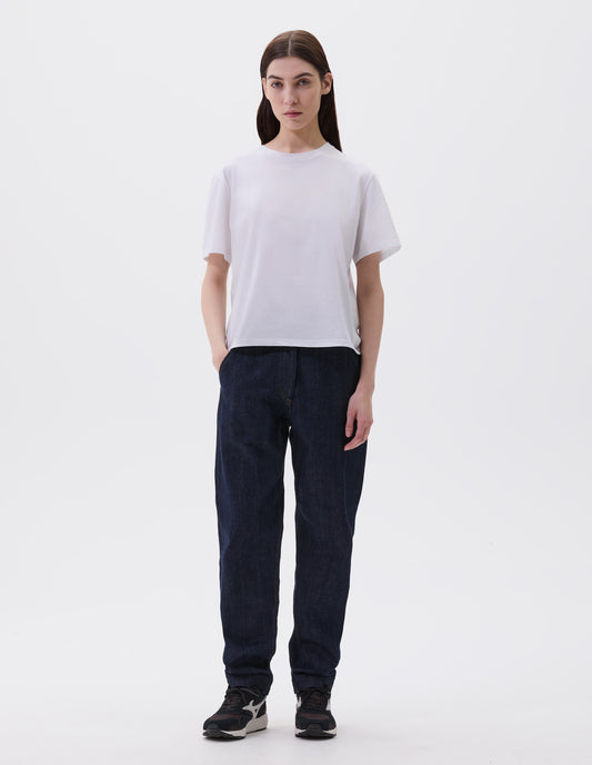 Full body image, front view of model wearing off white cotton short sleeve t-shirt with boxy cut, Styled with indigo blue denim jeans and black and brown trainers.