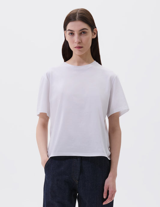 Cropped body image, front view of model wearing off white cotton short sleeve t-shirt with boxy cut, Styled with indigo blue denim jeans.