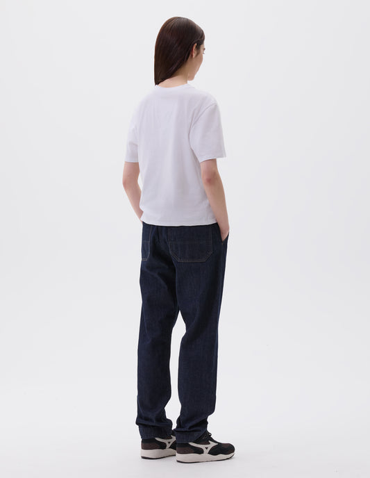 Full body image, back view of model wearing off white cotton short sleeve t-shirt with boxy cut, Styled with indigo blue denim jeans and black and brown trainers.