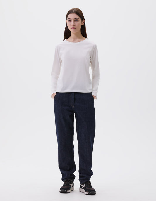 Full body image, front view of model wearing off white cotton wide neck long sleeve with boxy cut. Styled with indigo blue denim jeans and black and brown trainers. 