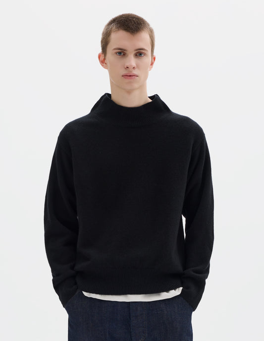 Cropped body image, front view of model wearing black fully fashioned seamless wool jumper with rib mock neck, set-in sleeves, and ribbed cuffs and hem. Styled over white t-shirt, and with dark blue jeans.