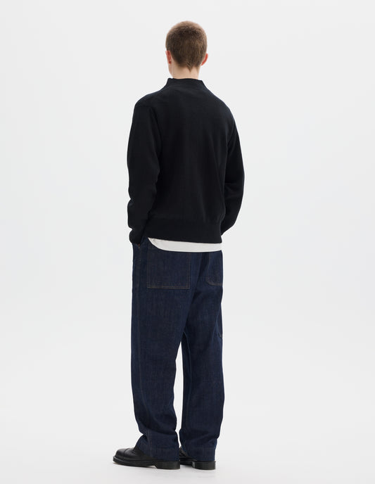 Full body image, back view of model wearing black fully fashioned seamless wool jumper with rib mock neck, set-in sleeves, and ribbed cuffs and hem. Styled over white t-shirt, and with dark blue jeans and black leather shoes.