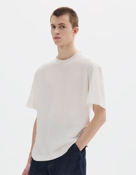 Cropped body image, front view of model wearing white relaxed cotton t-shirt with crew neck and boxy cut. Styled with dark blue jeans.