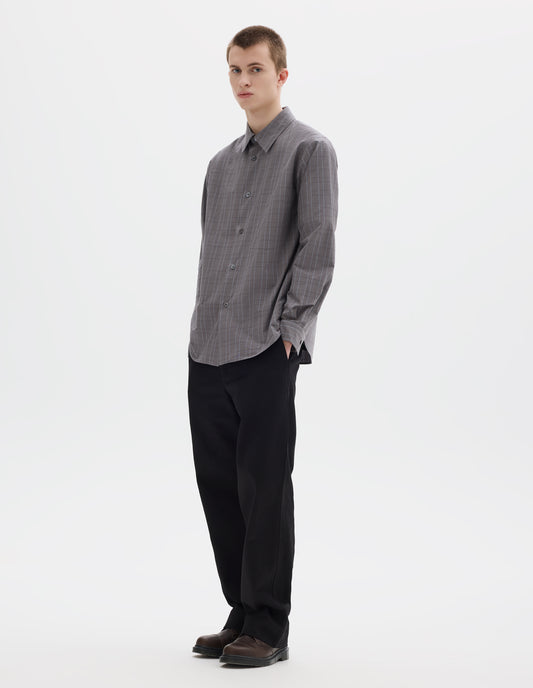 Full body image, front view of model wearing grey cotton shirt with dark grey and light blue checks, mother of pearl buttons and chest pocket. Styled with black trousers and brown leather shoes.