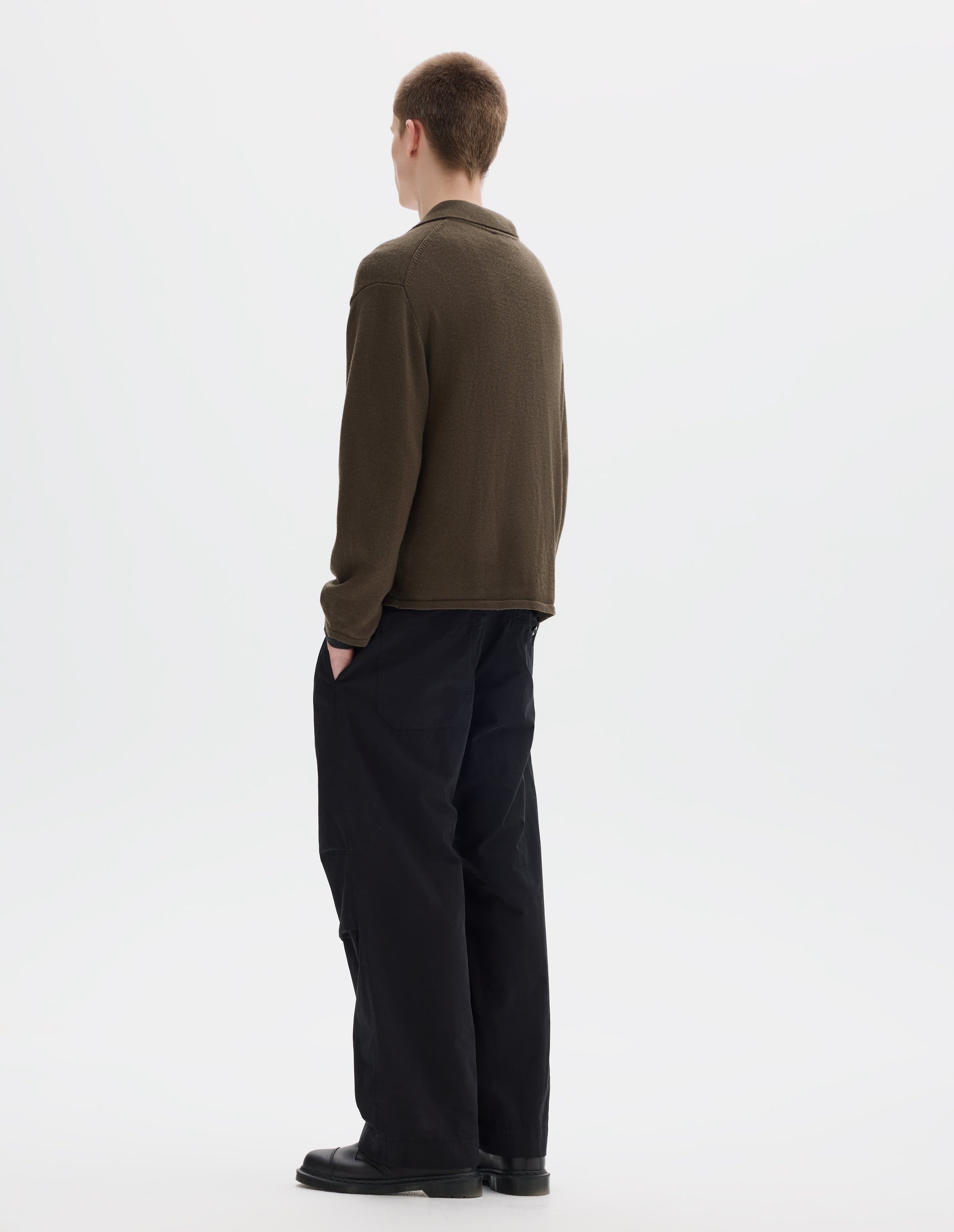 Full body image, back view of model wearing relaxed green merino cardigan with jersey stitch, fully fashioned collar, set-in fully fashioned sleeves, and tubular hem and cuffs. Styled with black trousers and black leather shoes.