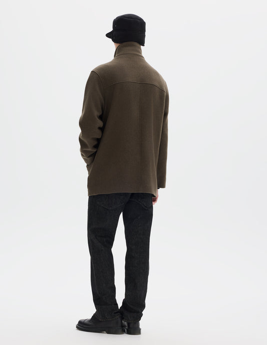 Full body image, back view of model wearing khaki green relaxed wool coat with half mock collar, back yoke and centre back seam. Styled with black shearling cap, black jeans and black leather shoes. 