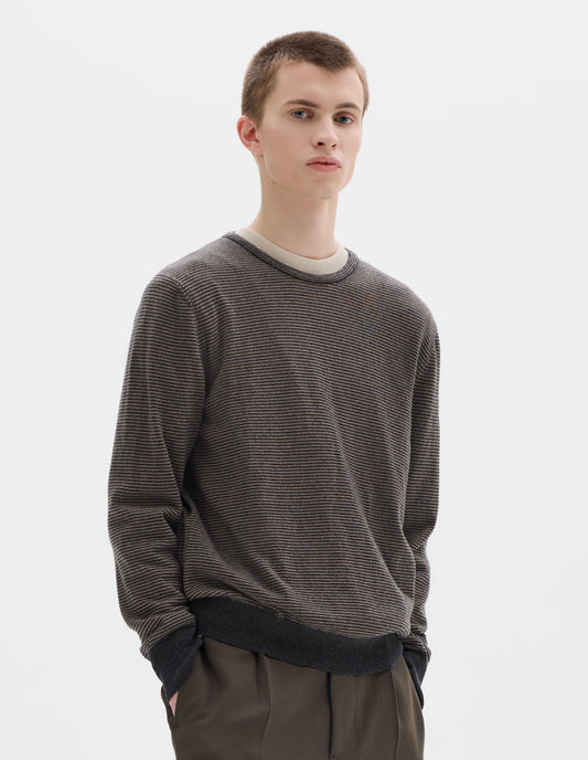 Cropped body image, front view of model wearing grey merino cashmere jumper with dark grey stripes, crew neck with tubular collar, and with contrast rib on cuffs and hem. Styled over white t-shirt and with khaki green trousers.