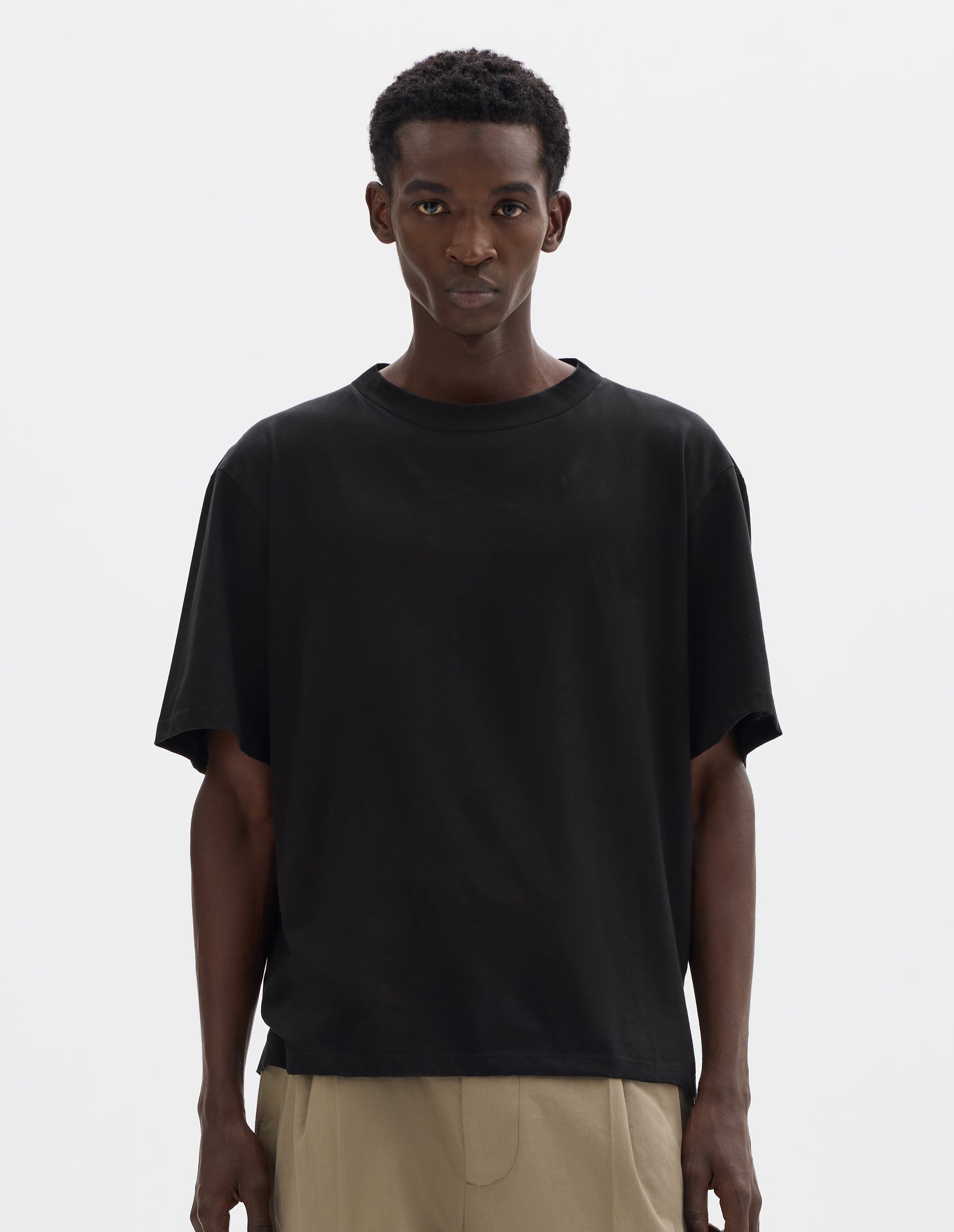 Cropped body image, front view of model wearing black relaxed cotton t-shirt with crew neck and boxy cut. Styled with beige trousers.