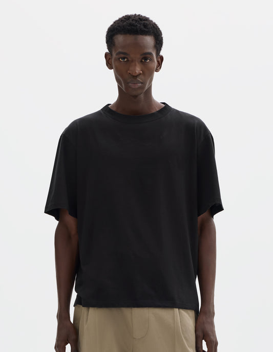 Cropped body image, front view of model wearing black relaxed cotton t-shirt with crew neck and boxy cut. Styled with beige trousers.