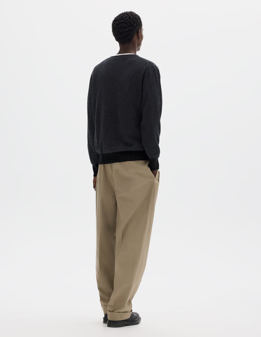Full body image, back view of model wearing dark grey merino cashmere jumper with black stripes, crew neck with tubular collar, and with contrast rib on cuffs and hem. Styled over white t-shirt and with beige trousers and black leather shoes.