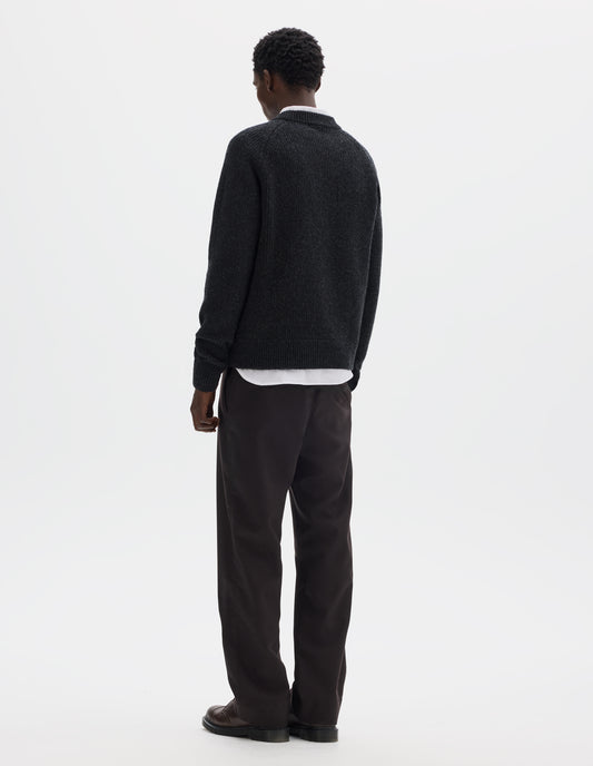 Full body image, back view of model wearing dark grey wool jumper with raglan sleeves, tubular collar and rib detailing at hem and cuffs. Styled over white shirt, and with brown trousers and brown leather shoes.