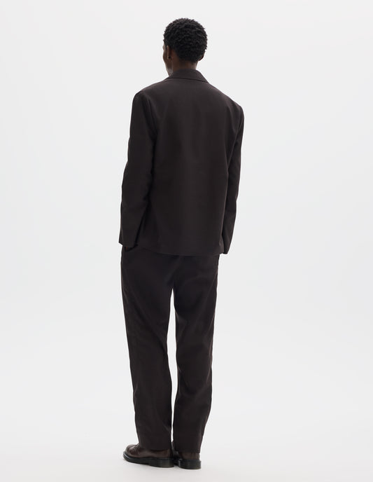 Full body image, back view of model wearing dark brown relaxed wool blazer with dropped shoulders. Styled with matching trousers and brown leather shoes.