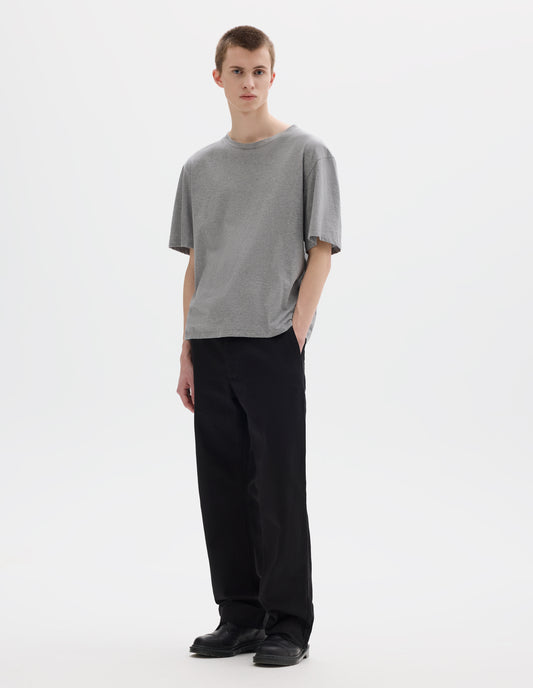 Full body image, front view of model wearing grey relaxed cotton t-shirt with crew neck and boxy cut. Styled with black trousers and black leather shoes.