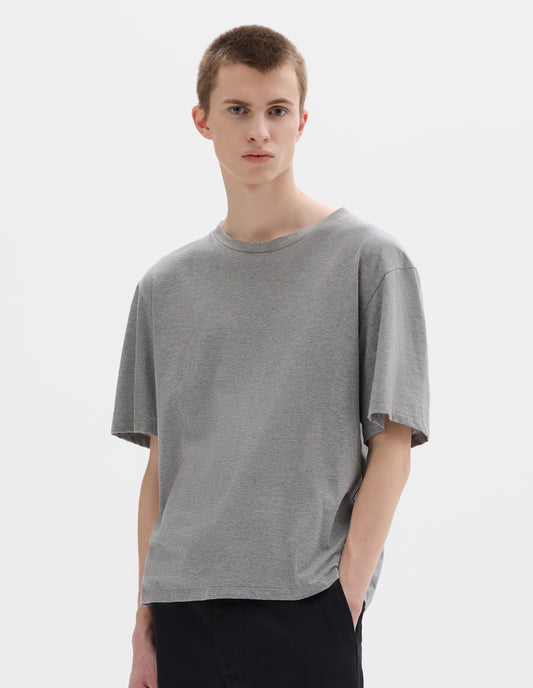 Cropped body image, front view of model wearing grey relaxed cotton t-shirt with crew neck and boxy cut. Styled with black trousers.
